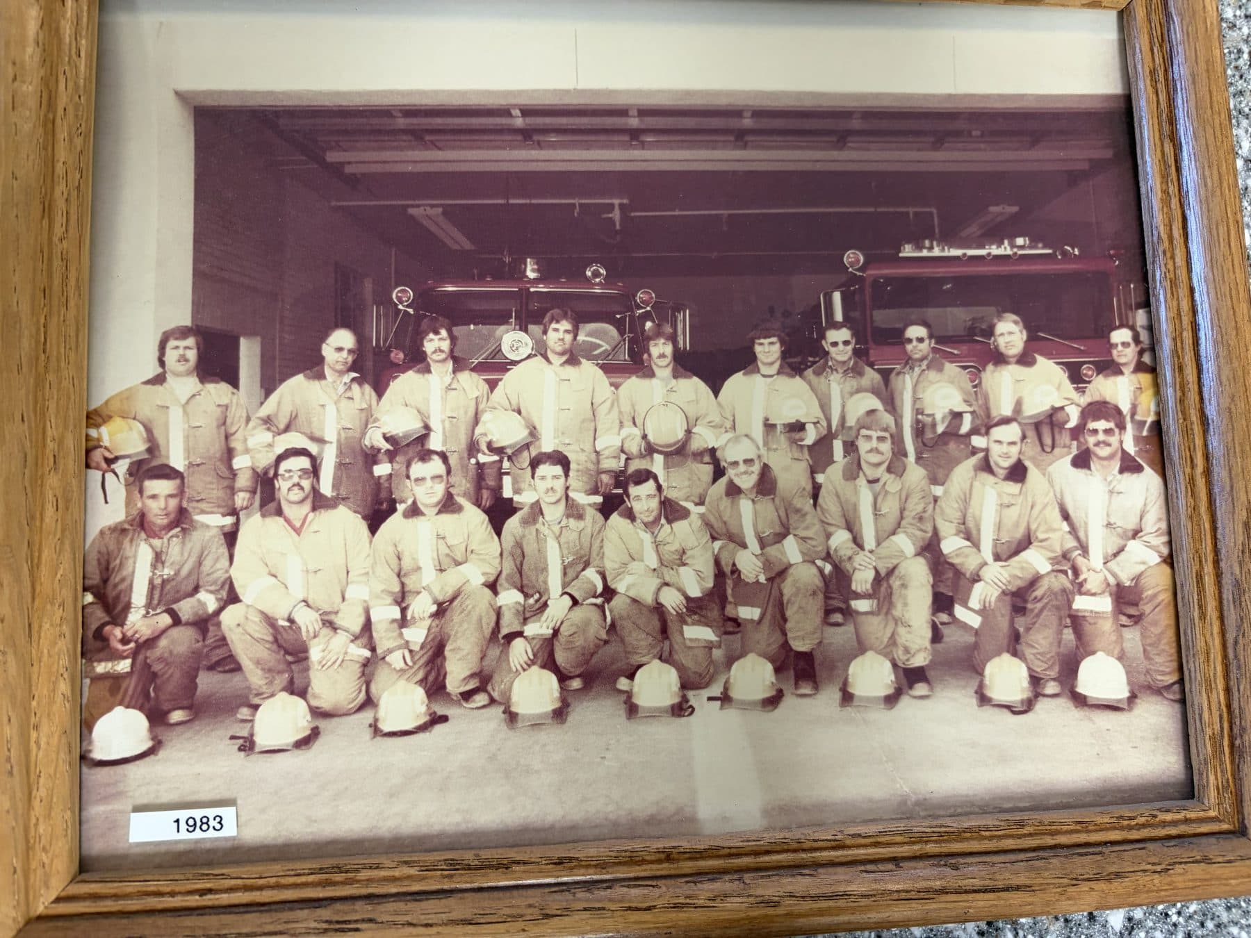 1983 Payette firefighters in tan turnout coats and helmets posed in the apparatus bay