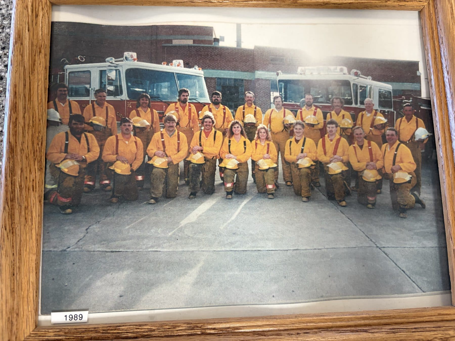 1989 Payette firefighters in orange turnout coats lined up in front of fire engines outside the station