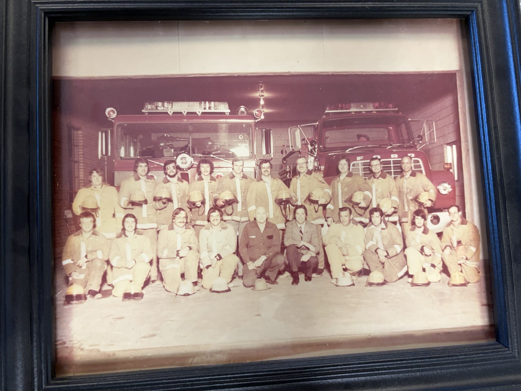 Undated vintage Payette crew photo in tan turnout coats in front of two engines inside the station
