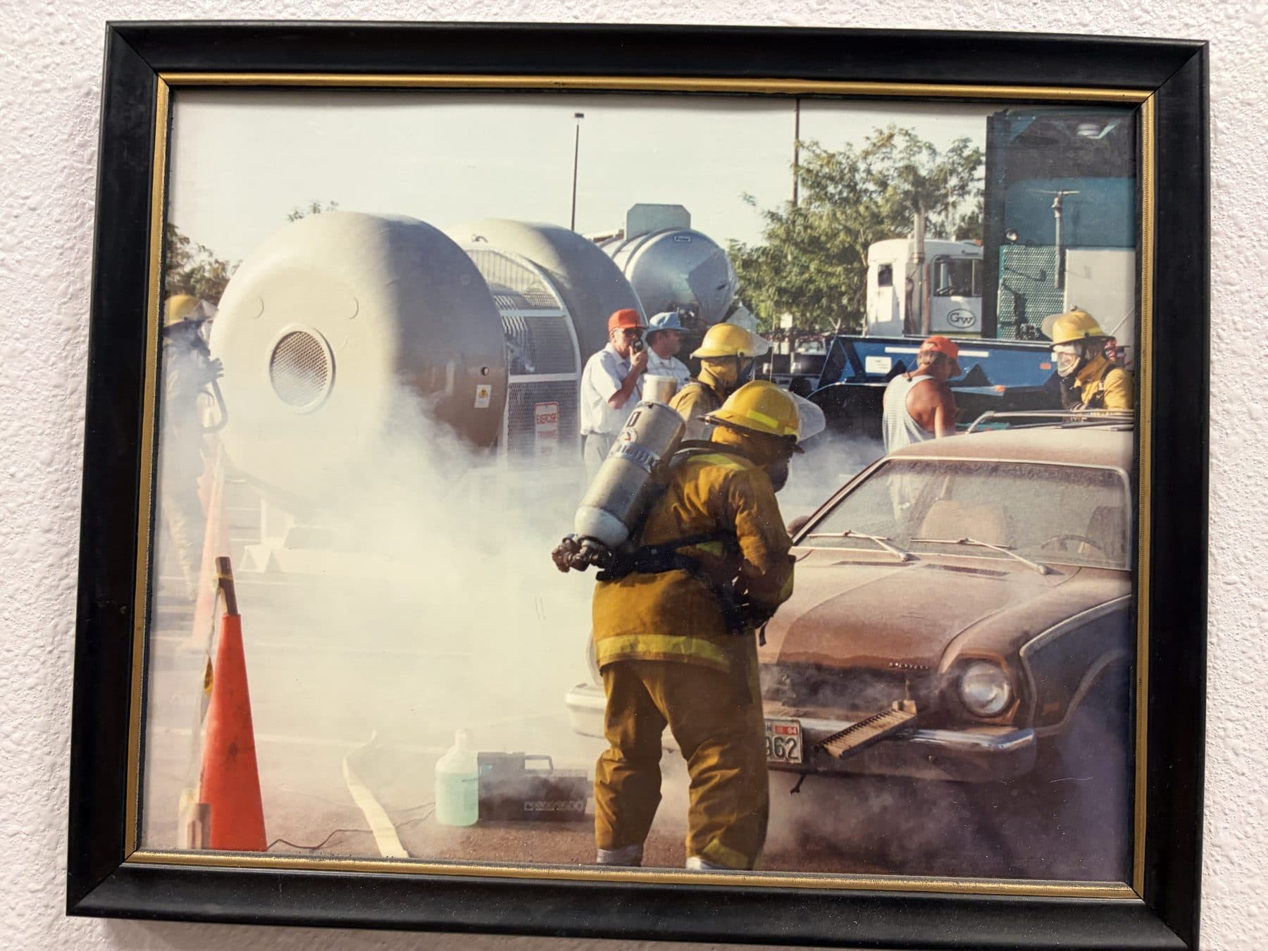 Vintage photo of Payette firefighters in yellow turnouts training with foam around a car and tanker at a hazmat scene