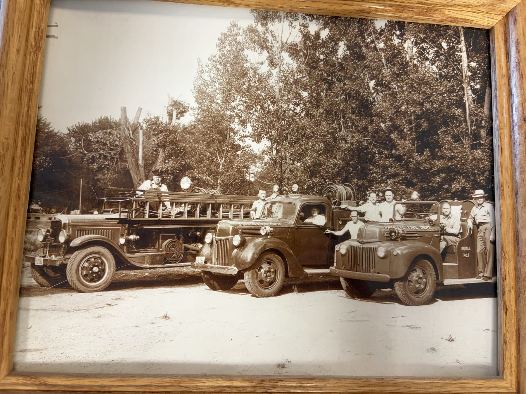 Sepia photograph of two early Payette fire engines parked under trees with crew aboard