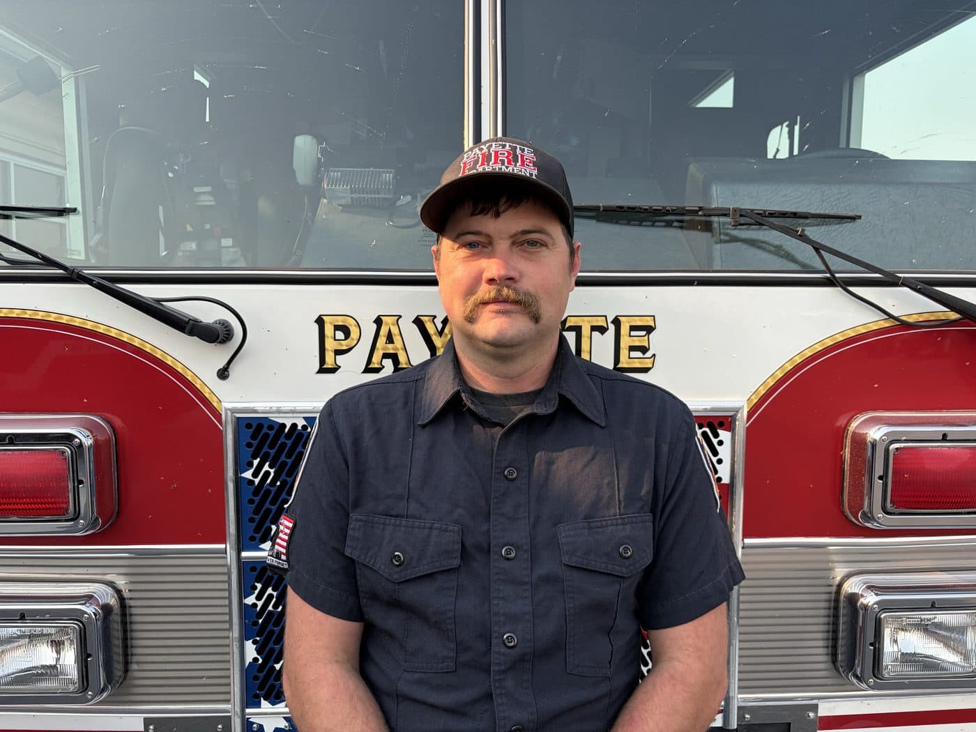 Engineer and EMT Shane Miller in uniform, standing in front of a Payette fire engine.
