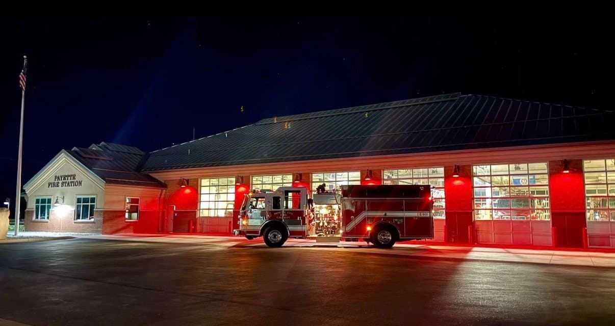 The Payette Fire Station at night, engine parked out front and the apparatus bays lit red behind it